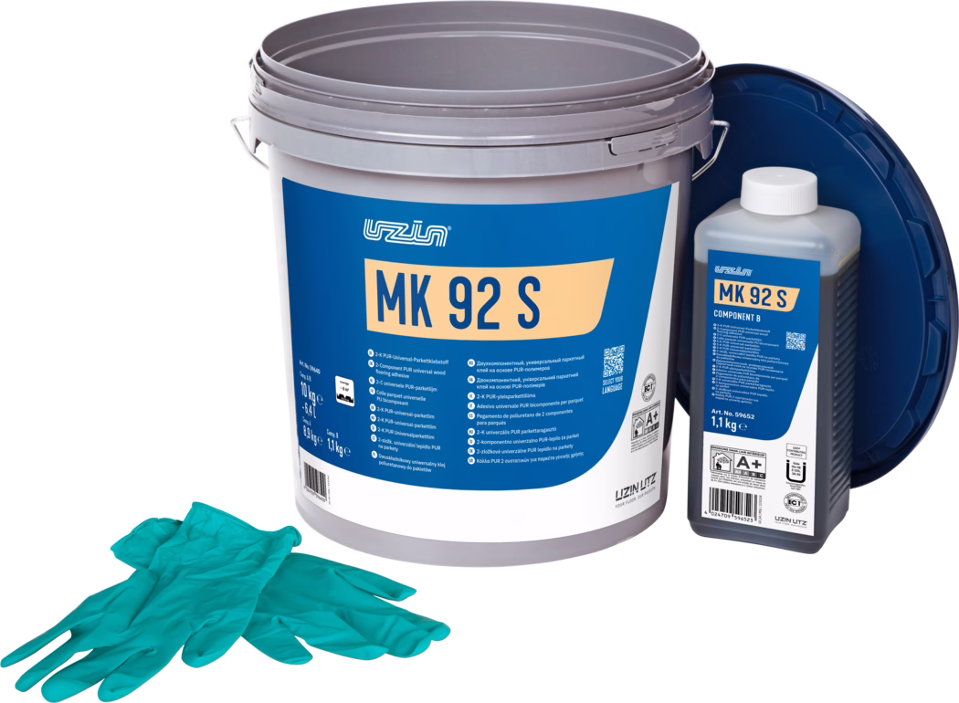 UZIN_Dummy_MK 92 S-10kg_2024-09 Studio-Produktfoto eines Parkettkleber-Sets: Ein großer grauer Kunststoffeimer mit einem markanten blauen Etikett mit der Aufschrift 'MK 92 S', daneben rechts eine kleinere rechteckige Flasche mit der Aufschrift 'MK 92 S Component B' und weißer Verschlusskappe; ein dunkler blauer Deckel lehnt im Hintergrund. Im Vordergrund liegt ein Paar türkisfarbener Einweghandschuhe. Die Gegenstände stehen auf weißem Hintergrund und sind gleichmäßig beleuchtet, wobei Verpackungsdetails und Produktinformationen für die Bodenverlegung betont werden.